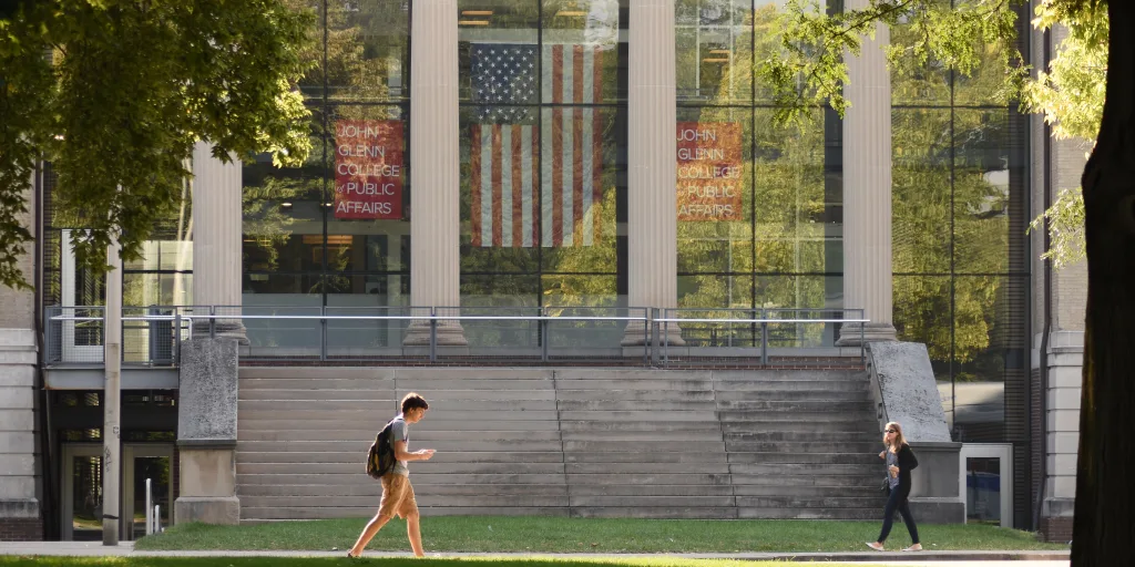 The glass entrance to John Glenn College with students walking in front.