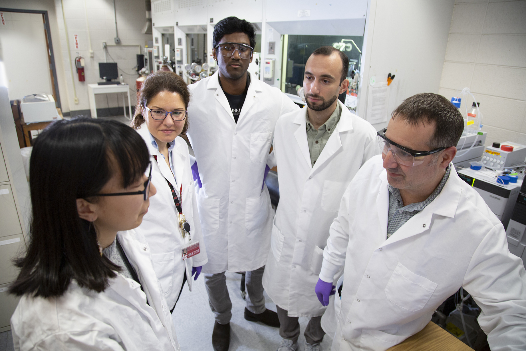 Group of students and instructors in lab coats discussing lab procedures