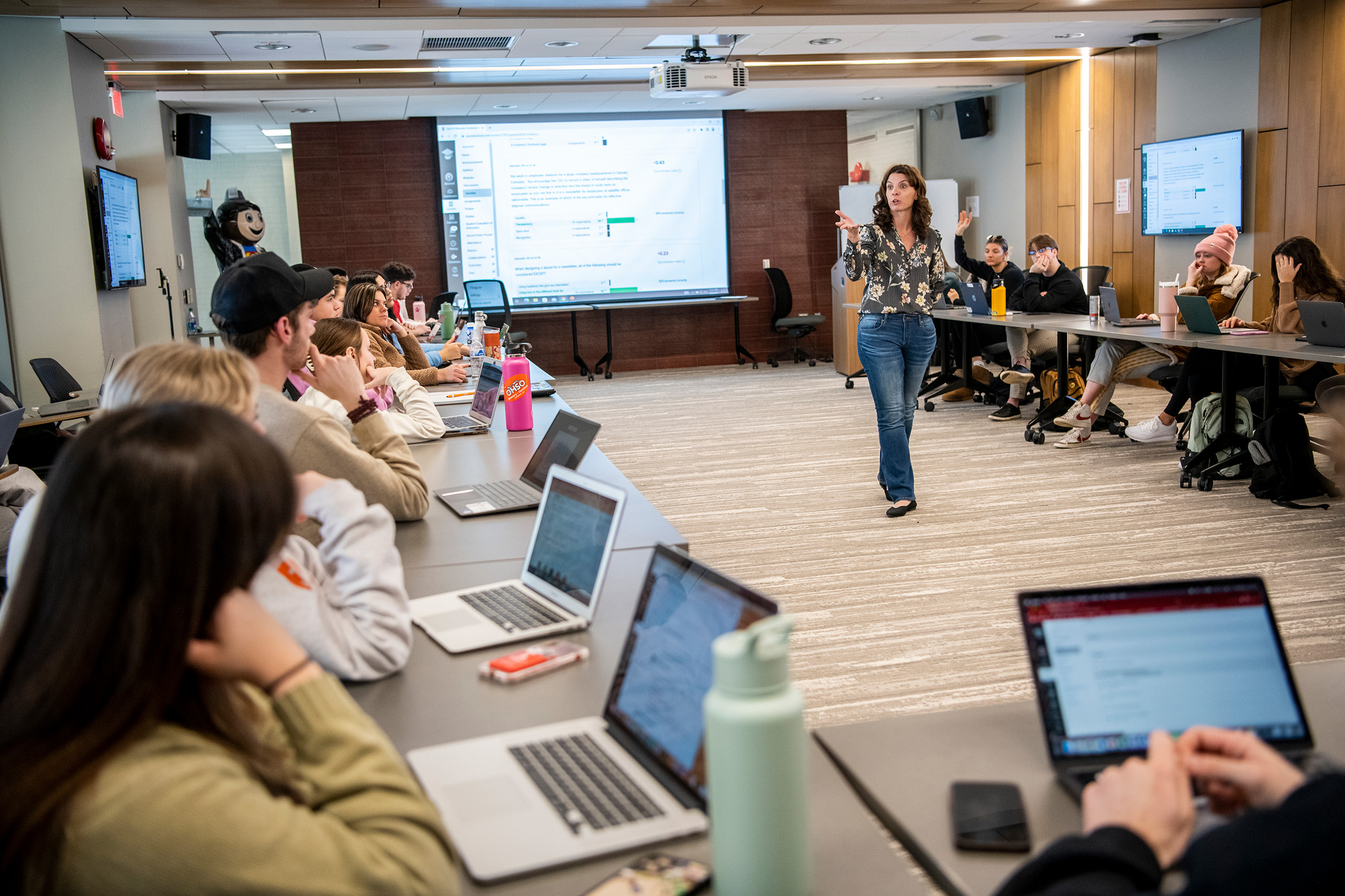 Professor lecturing in front of a classroom with students sitting in the round