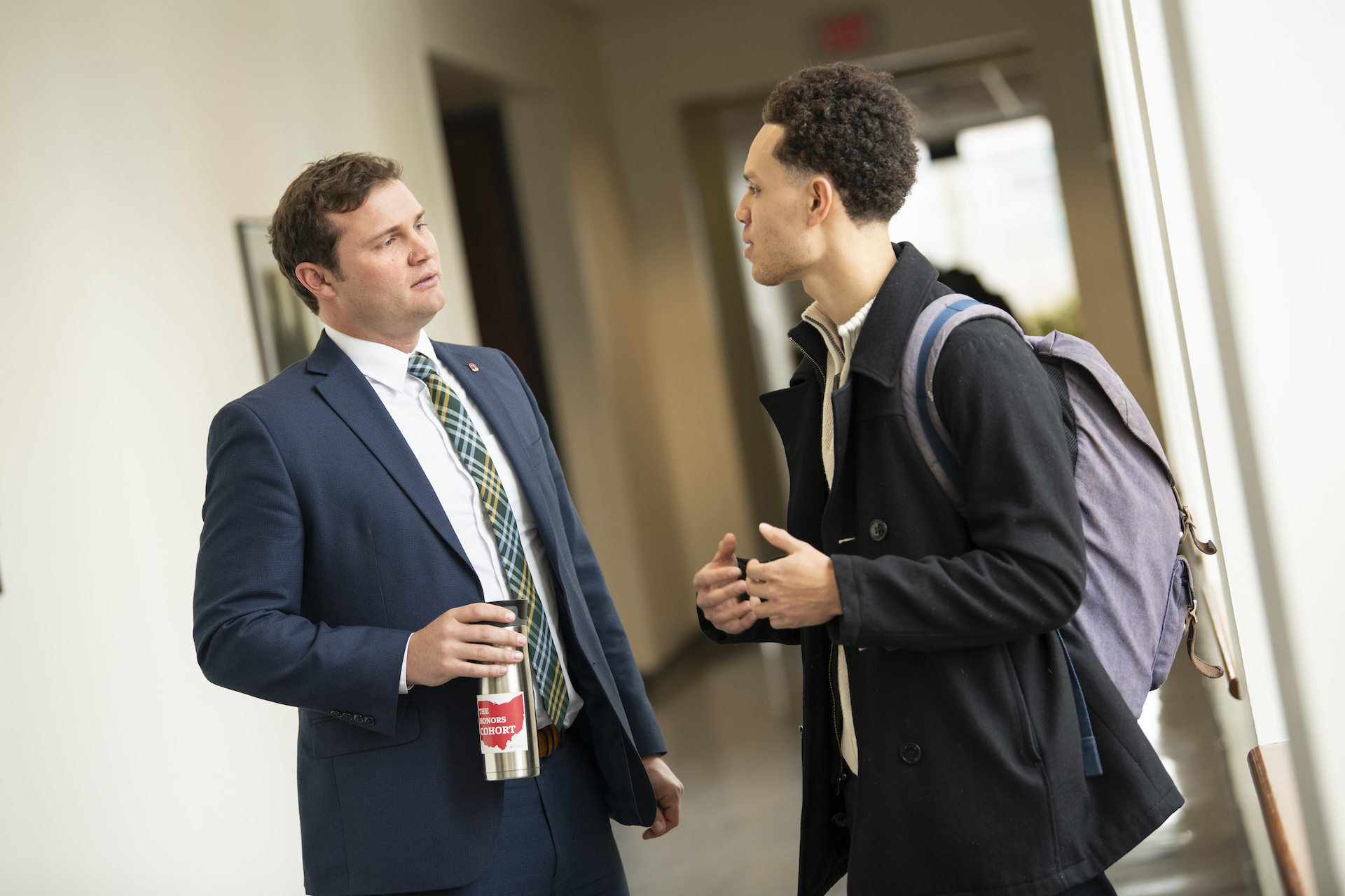 Two young men discuss something in a hallway.