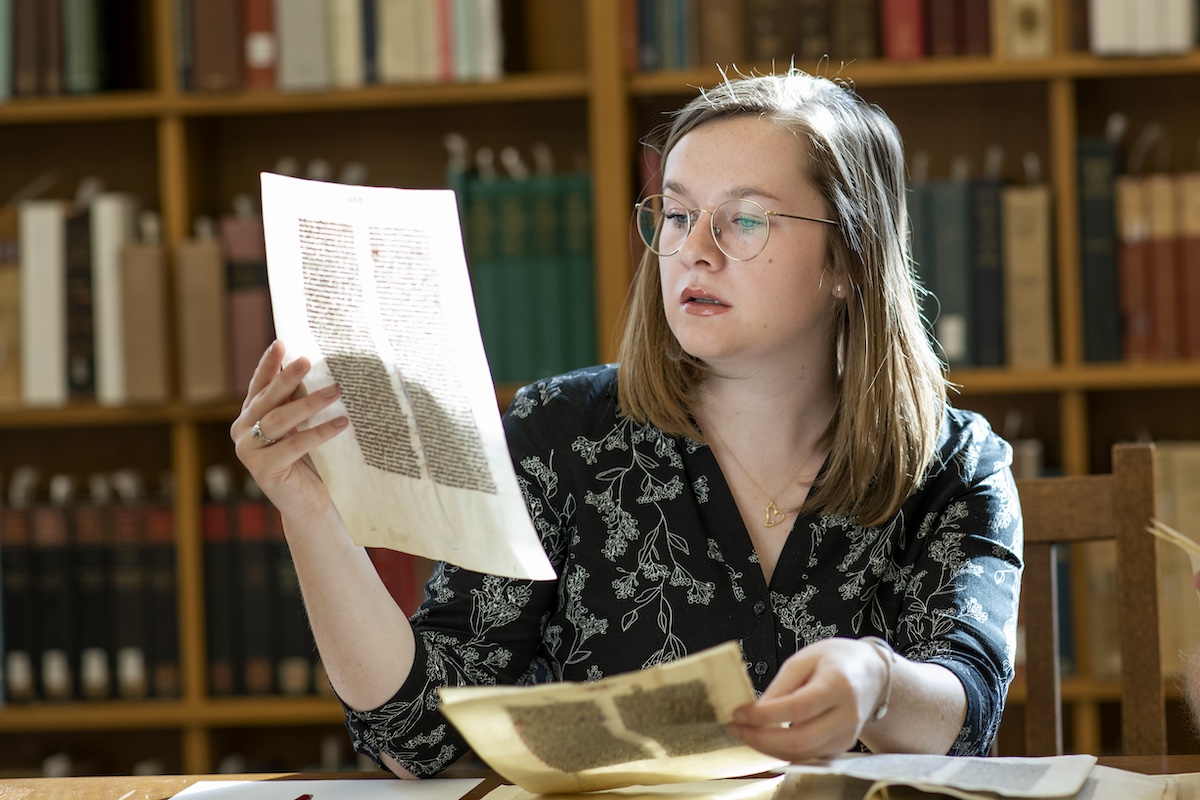 A woman sits in a library examining historical documents.