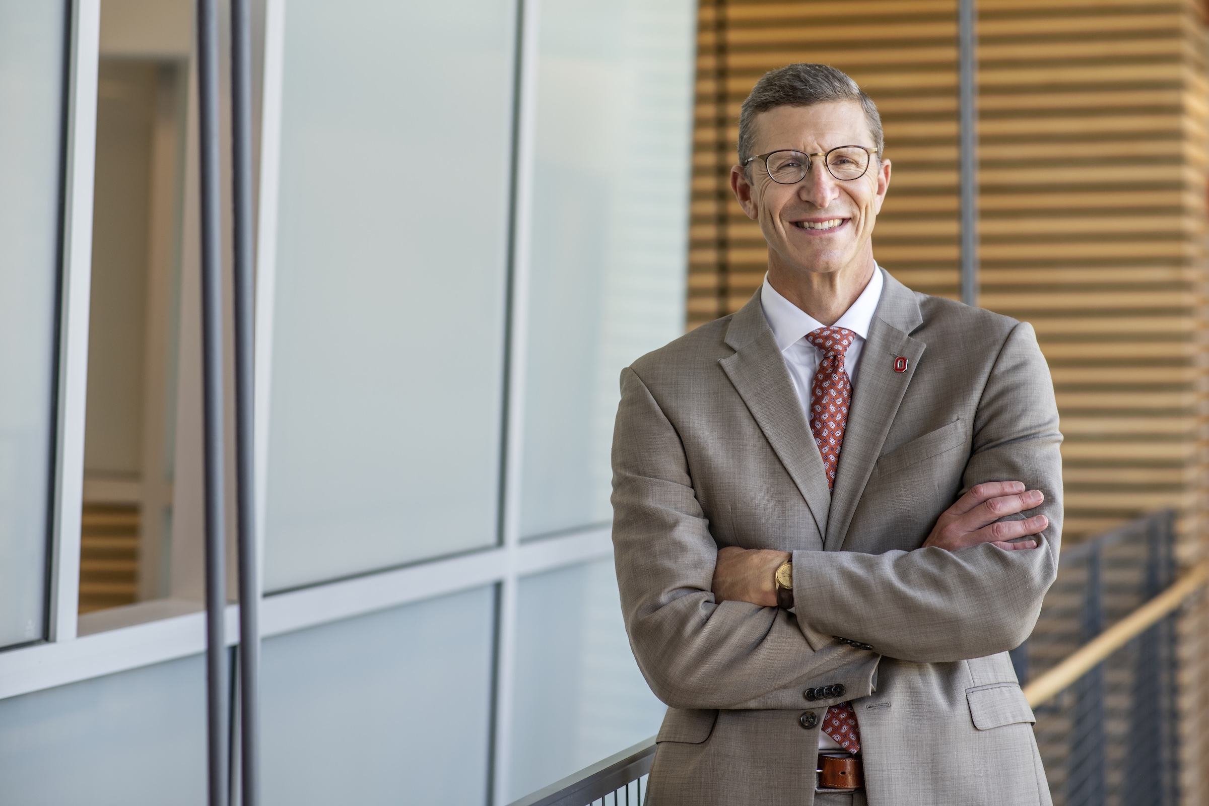 A portrait photo of Trevor Brown indoors, leaning against a rail with his arms crossed and a welcoming smile.