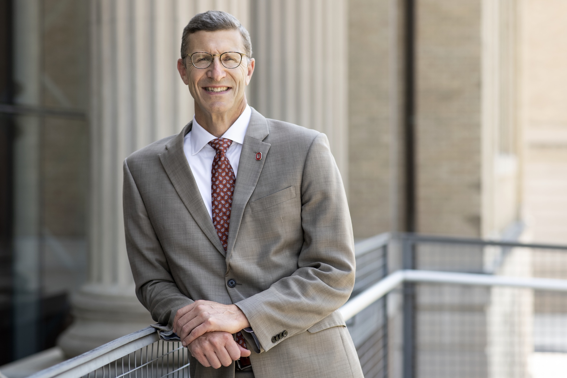 Trevor Brown leaning agains a railing on the outside of the John Glenn School. Close up shot with columns in the background.