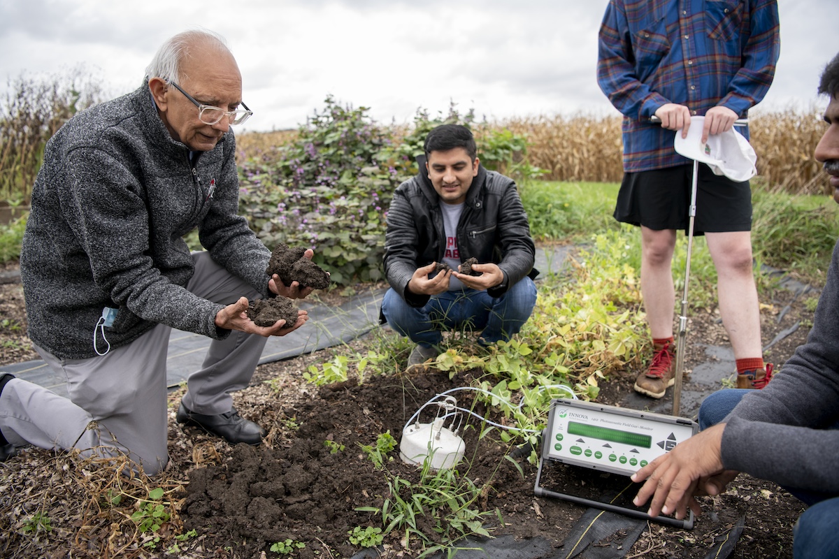 A professor and four three students work outside in a farm field testing soil.