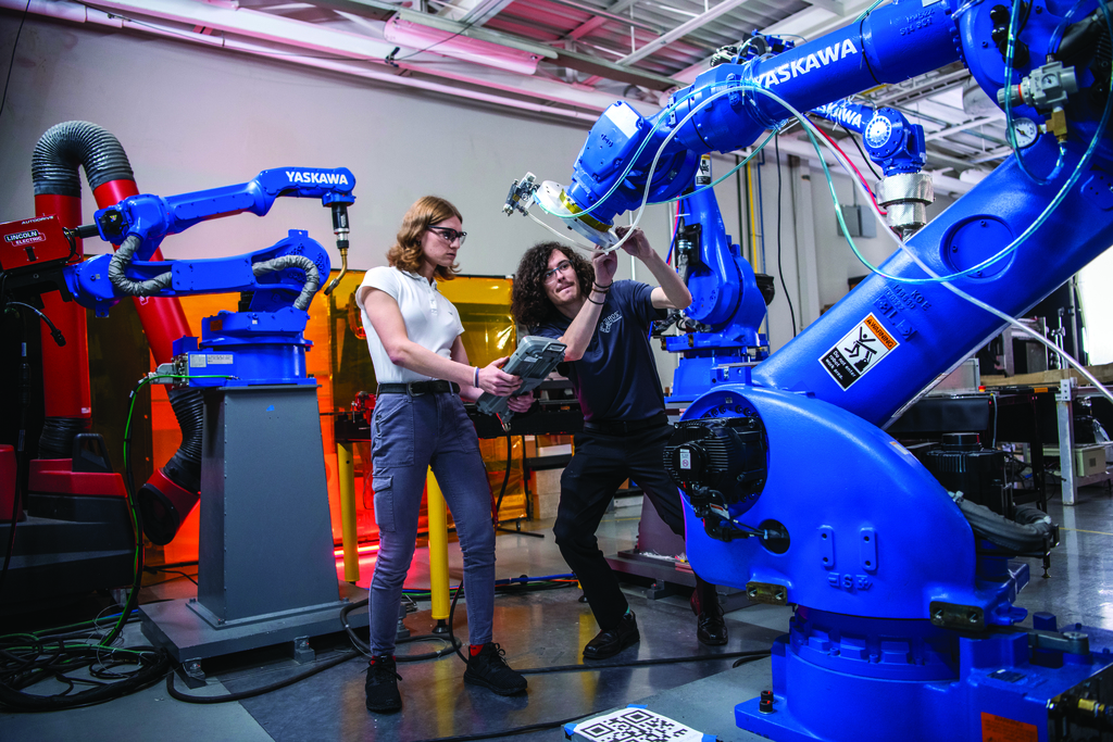 Two students work with a large robotic arm in a lab setting.