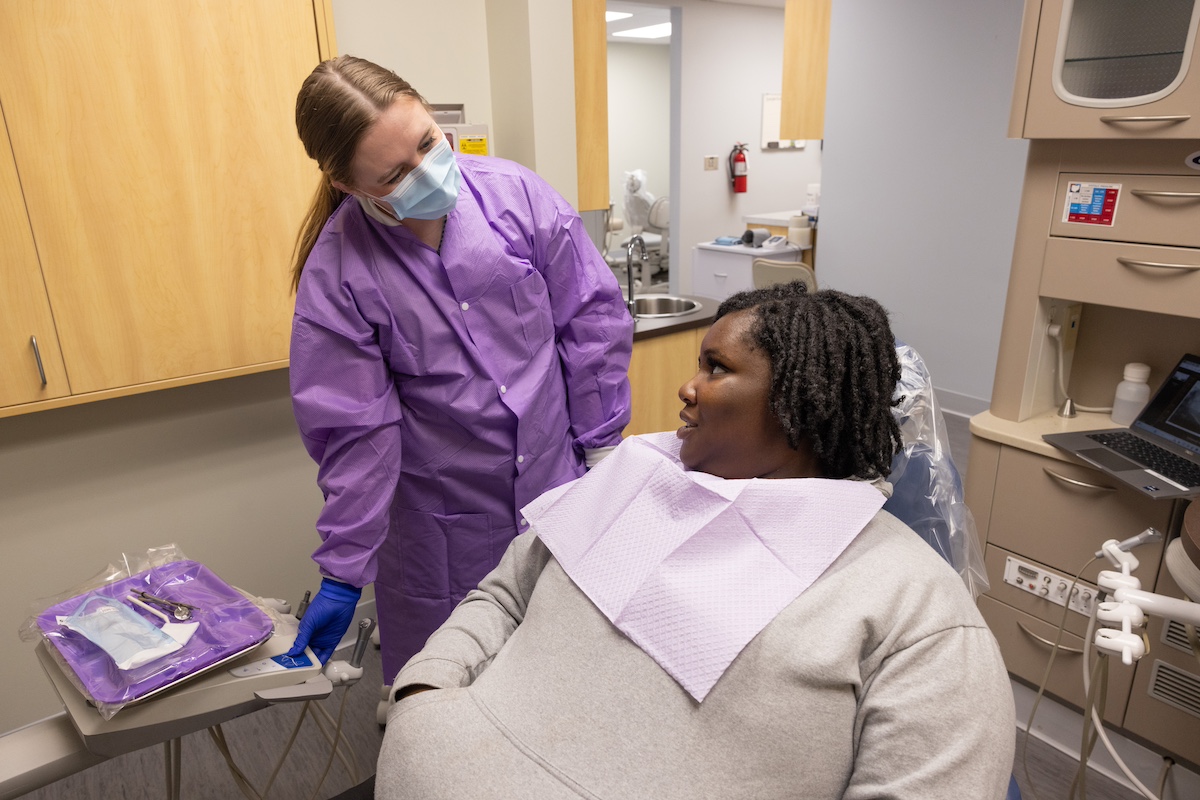 A dentistry student speaks with a patient in a clinical setting.