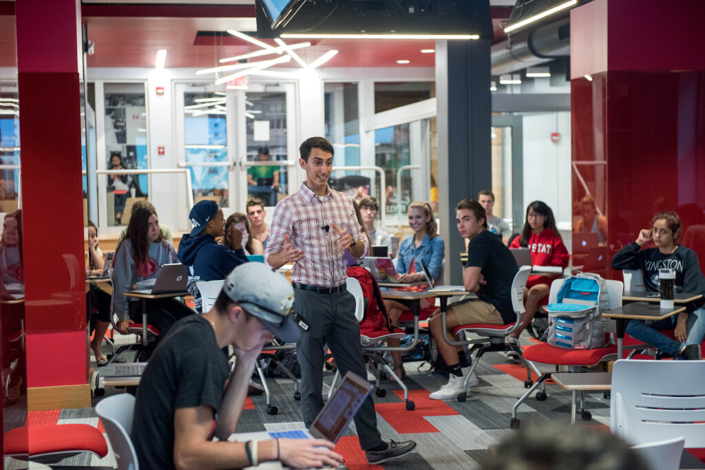 A lecturer stands in the middle of a seated class.