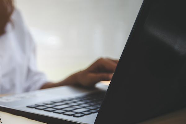 A young woman sits in front of a computer with a hand on the keyboard.