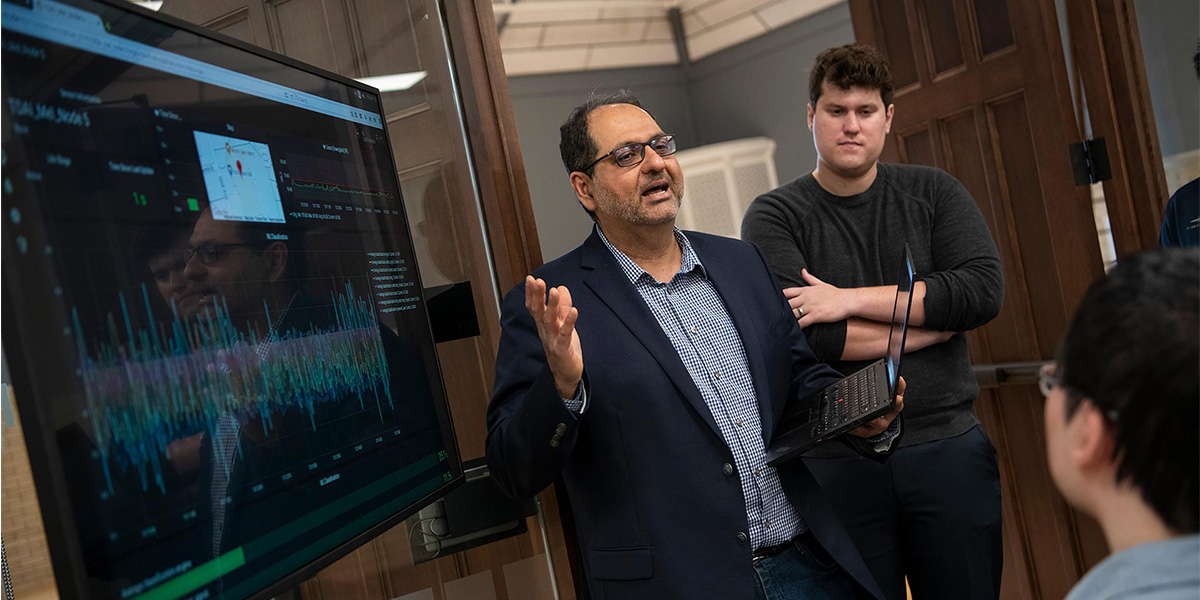 Faculty member speaking in front of a large screen to two students