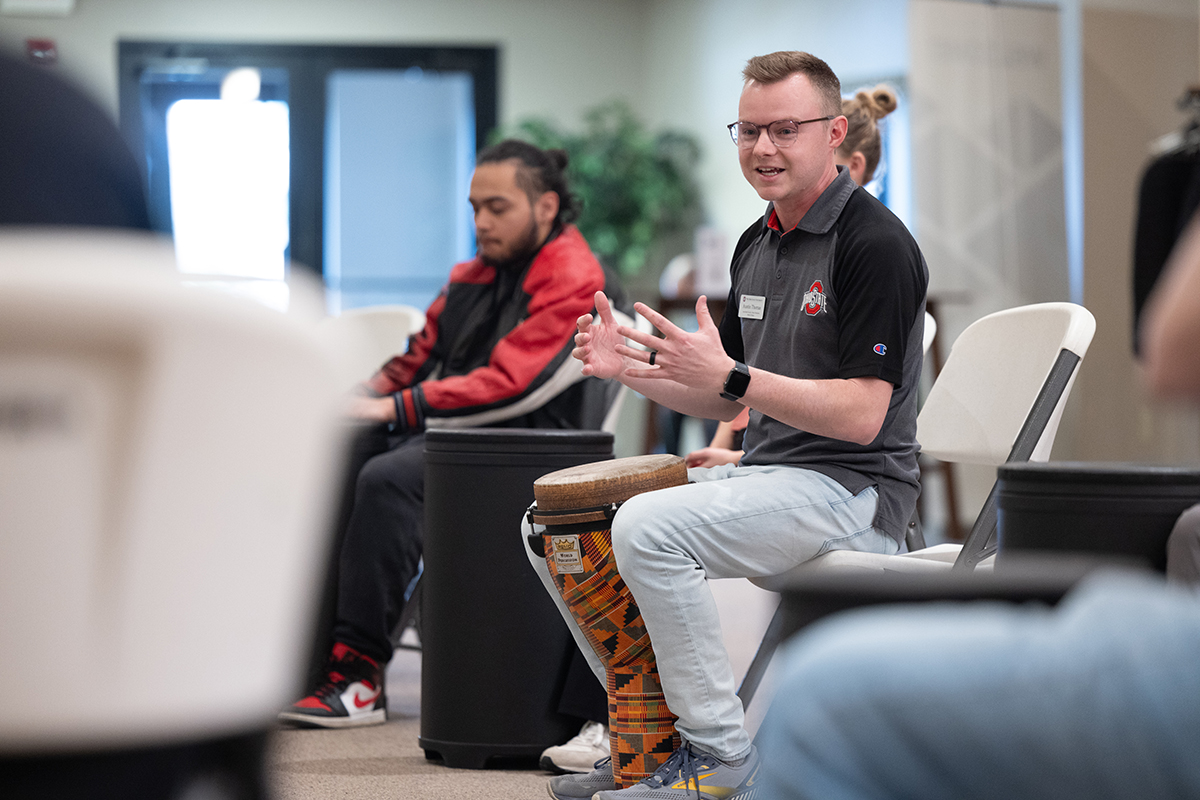 Two men playing drums with their hands in an indoor space.