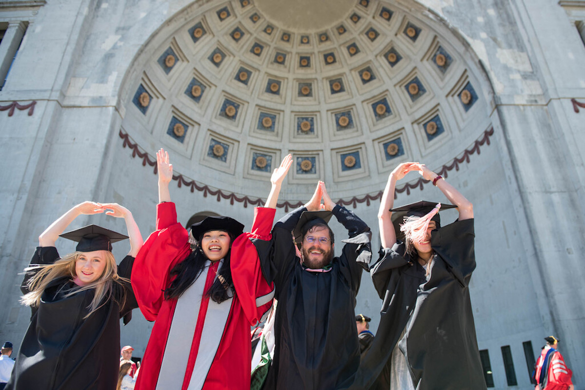 Picture of four students doing OHIO in front of Ohio Stadium on graduation day.