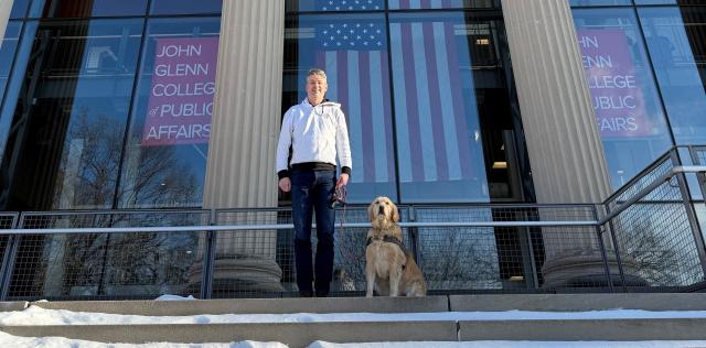 Ryan Brownfield stands next to his golden retriever, Mabel, outside the John Glenn College of Public Affairs.