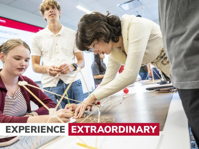 Students work around a model sitting on a table. Text on image reads "Experience Extraordinary"