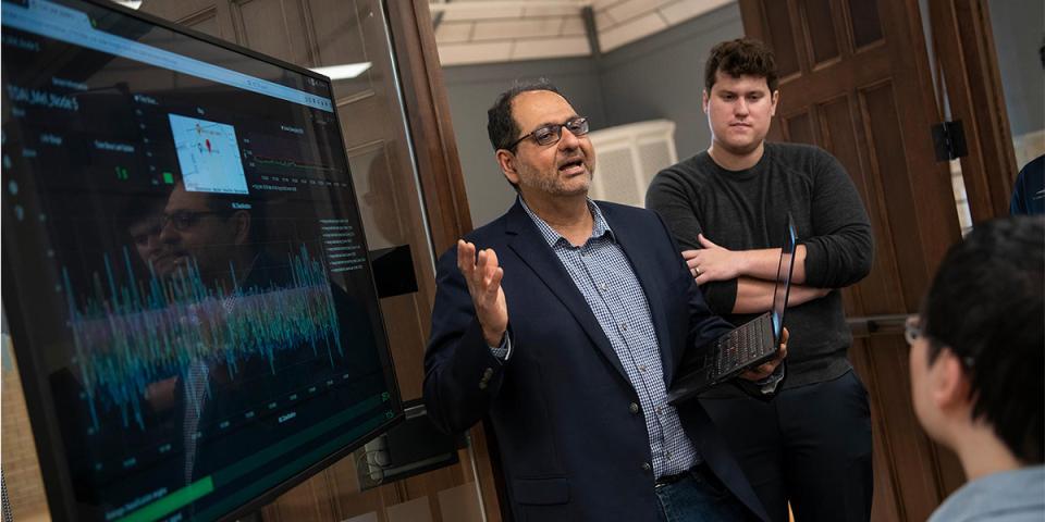 Faculty member speaking in front of a large screen to two students