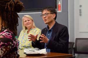 A faculty member speaks animatedly while another faculty member looks on.