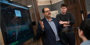 Faculty member speaking in front of a large screen to two students